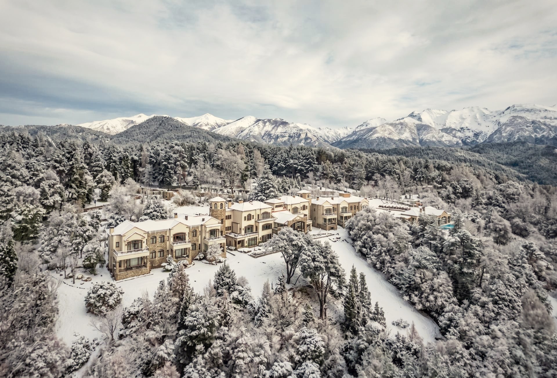 Aerial view of Villa Beluno luxury boutique hotel surrounded by snow-covered Patagonian forest and the Andes mountains in winter, Bariloche, Argentina