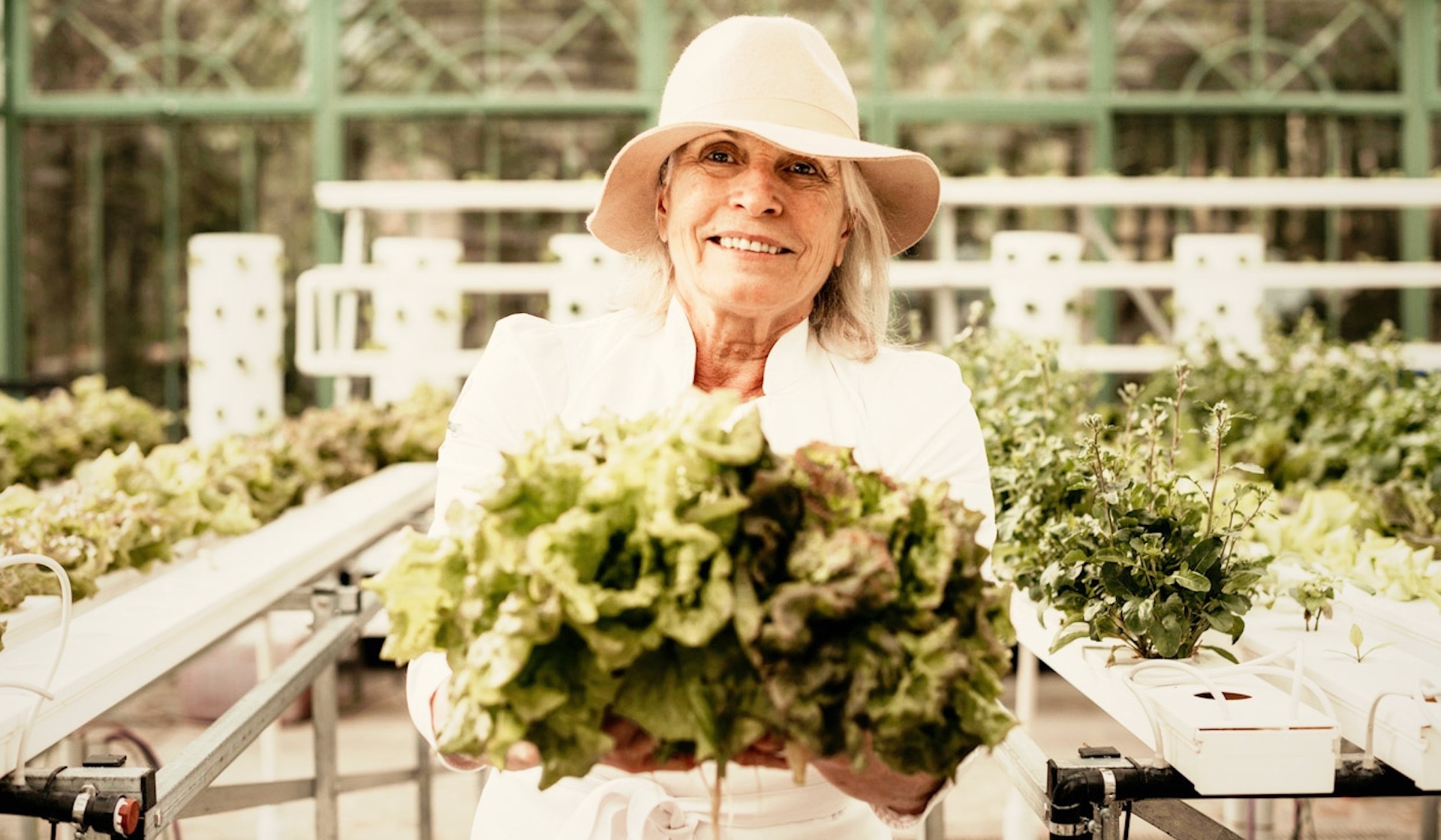 Head chef Cristina Lopez smiling with freshly harvested lettuce from Villa Beluno's hydroponic greenhouse, luxury boutique hotel in Bariloche, Patagonia